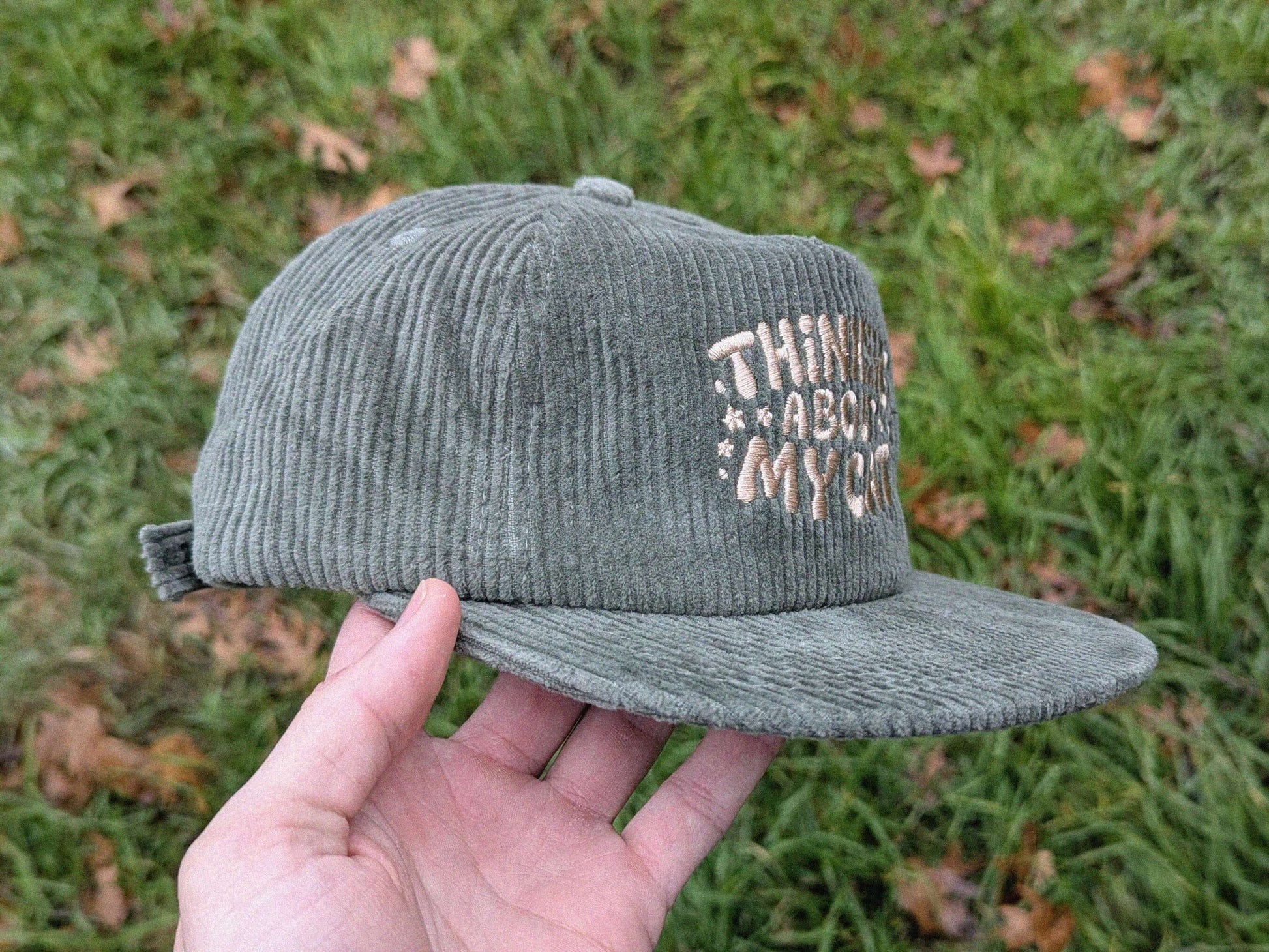 Green corduroy cap with text held in front of grass