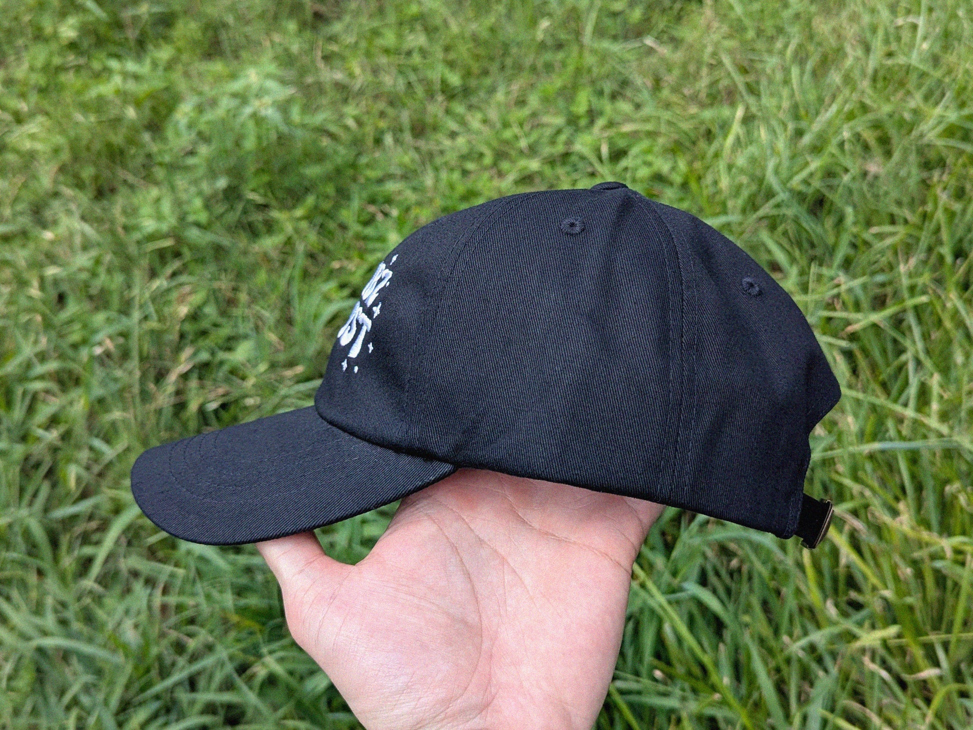 Black cap held in a hand with grass in the background