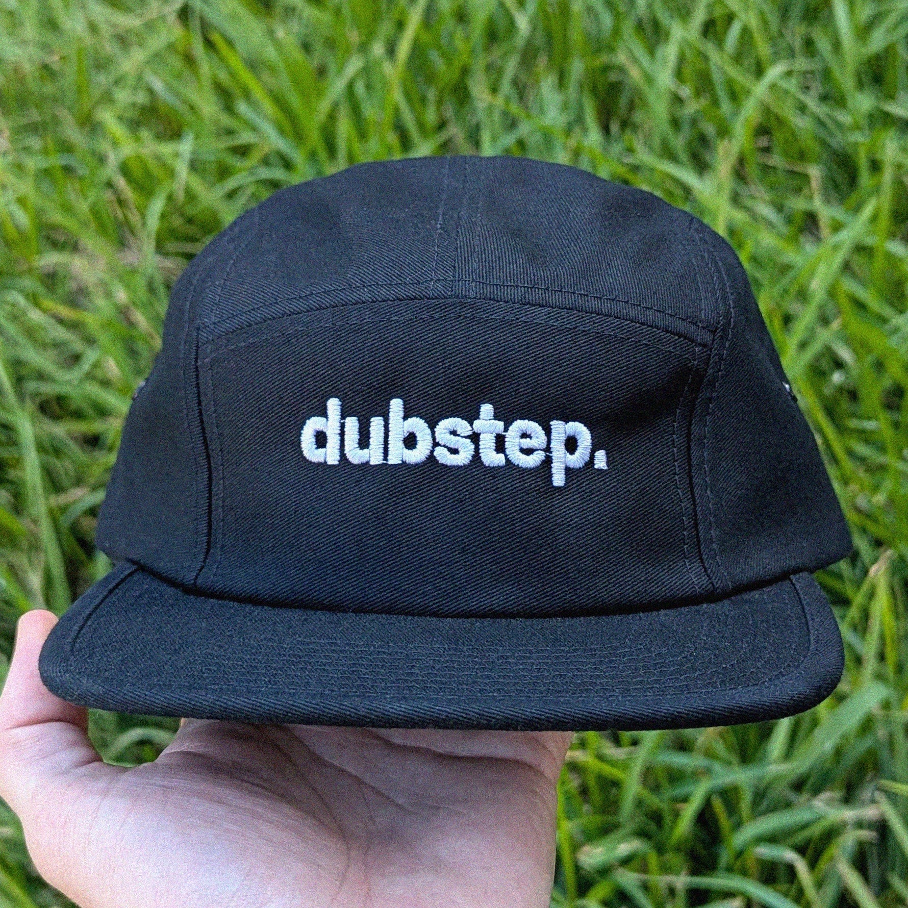 Black cap with 'dubstep.' text held in front of green grass
