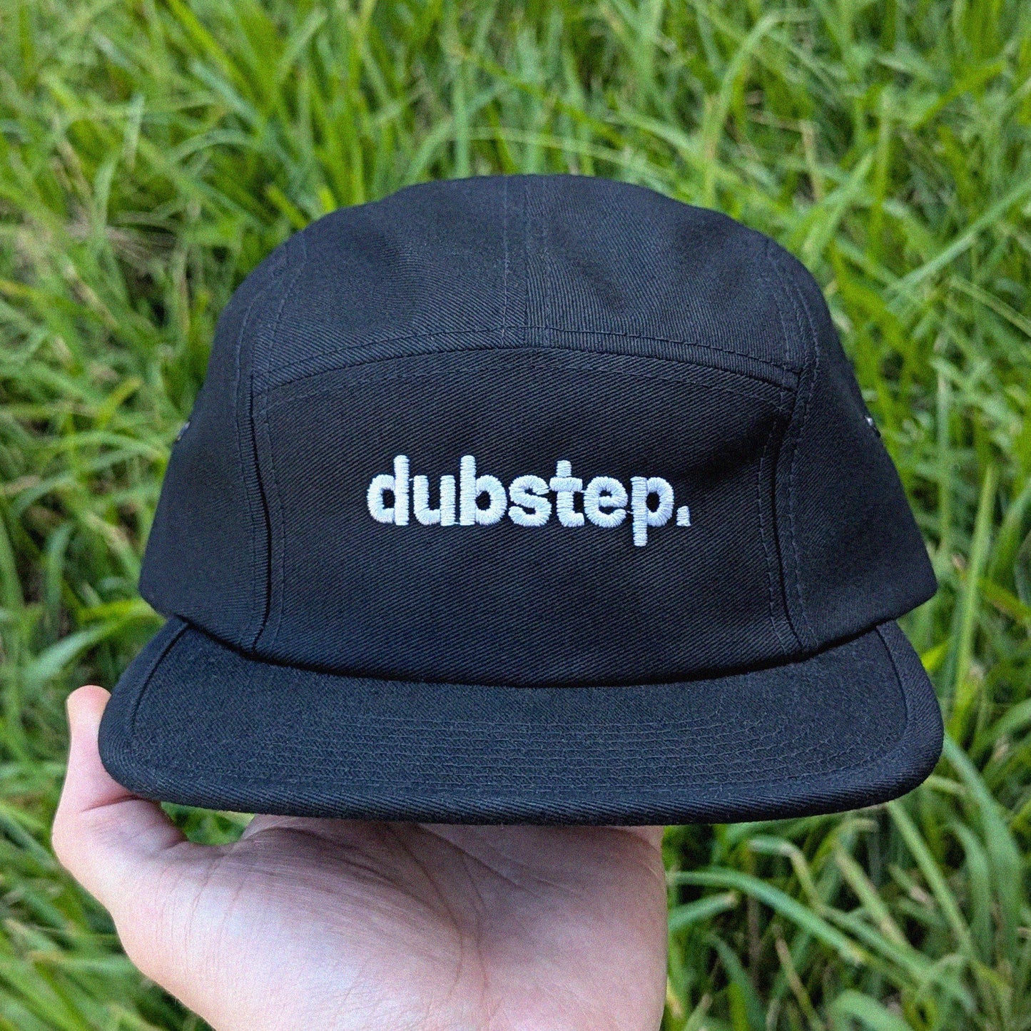 Black cap with 'dubstep.' text held in front of green grass