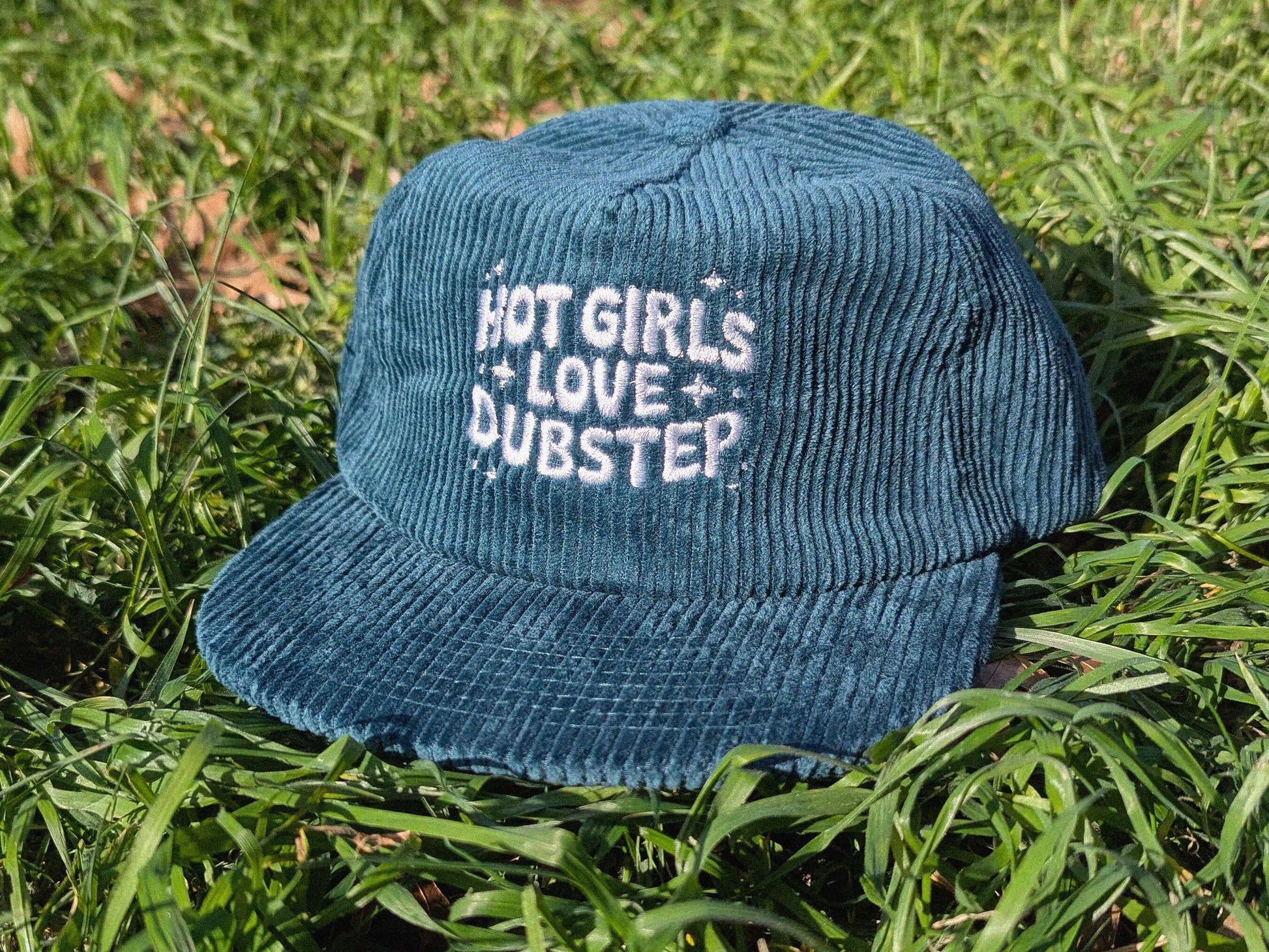 Teal corduroy hat with 'Hot Girls Love Dubstep' text on grass