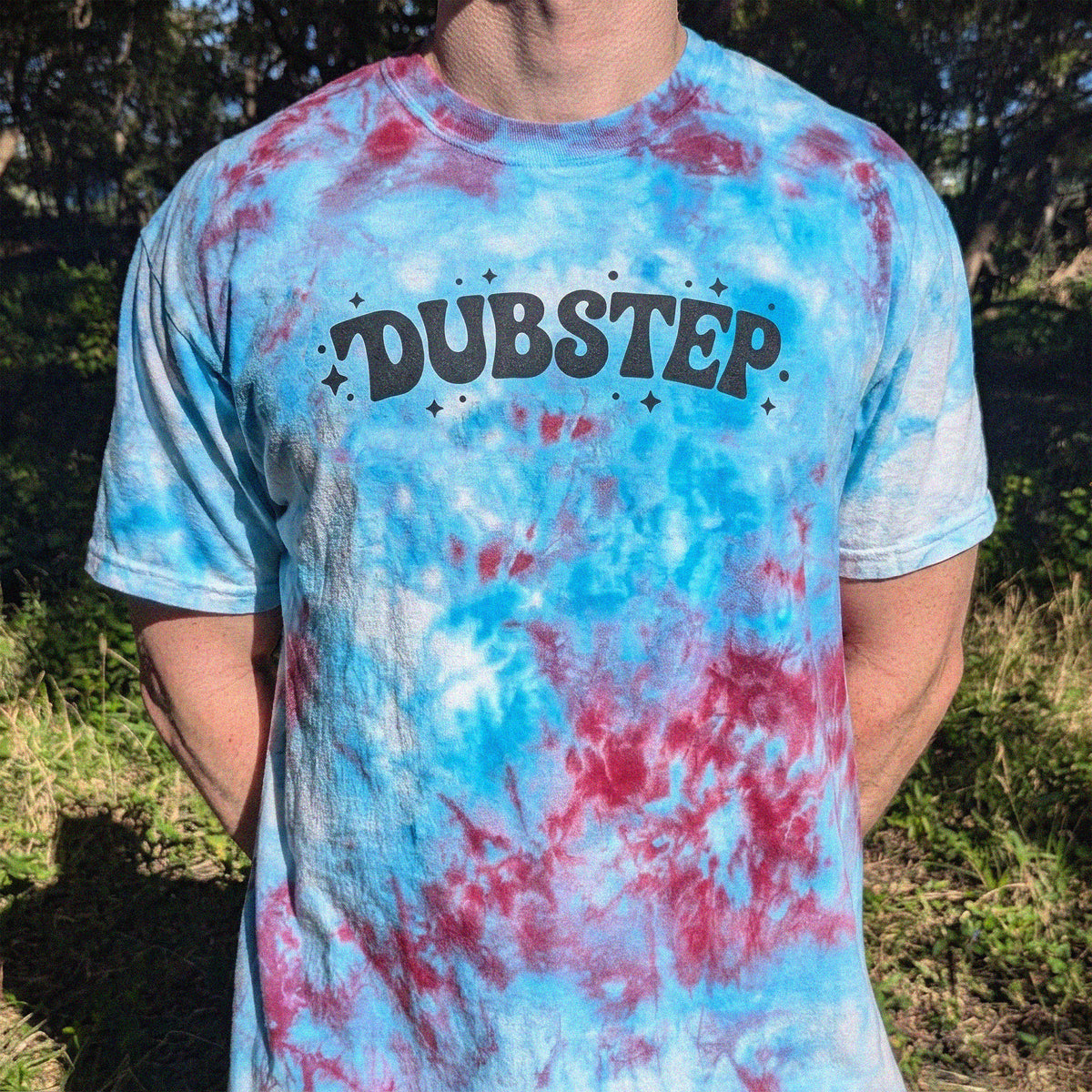 A person outdoors wearing a blue and pink tie-dye t-shirt with 'DUBSTEP' printed across the chest in black.