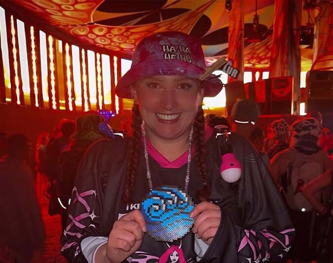 Person wearing a vibrant tie dye bucket hat with "HA HA HE HU" embroidery at a rave or music festival