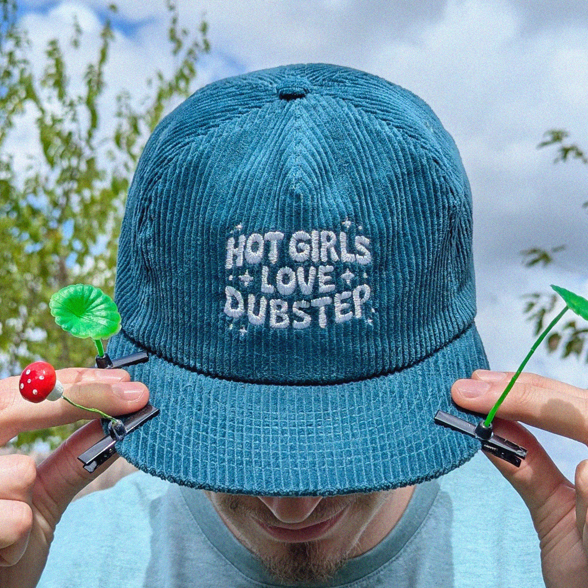 A man wearing a teal corduroy baseball cap with 'HOT GIRLS LOVE DUBSTEP' embroidered in white on the front.