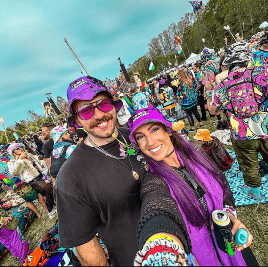 Couple wearing vibrant bucket hats at a colorful rave with festival attendees in the background.