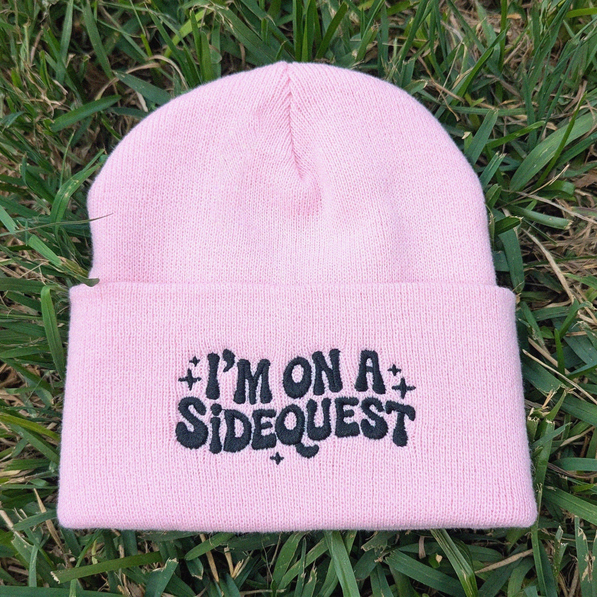 Pink beanie with 'I'm on a sidequest' text on grass