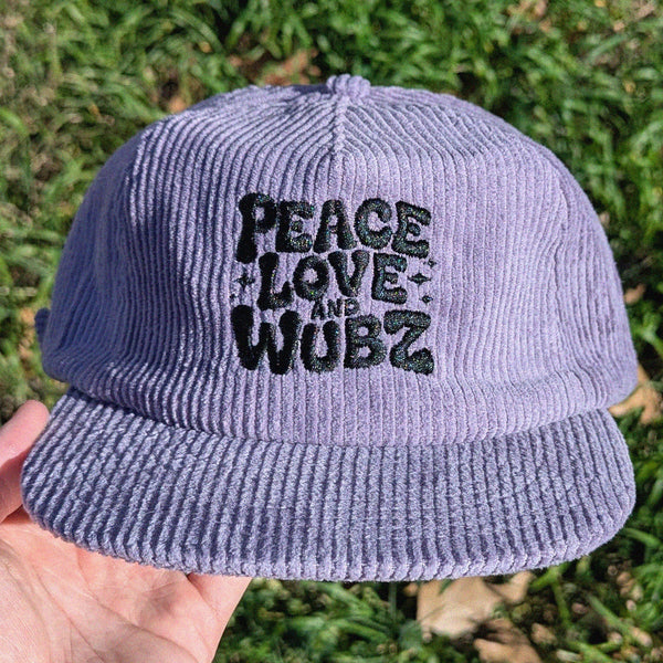 Purple corduroy cap with 'Peace Love and Wubz' text held in front of grass.