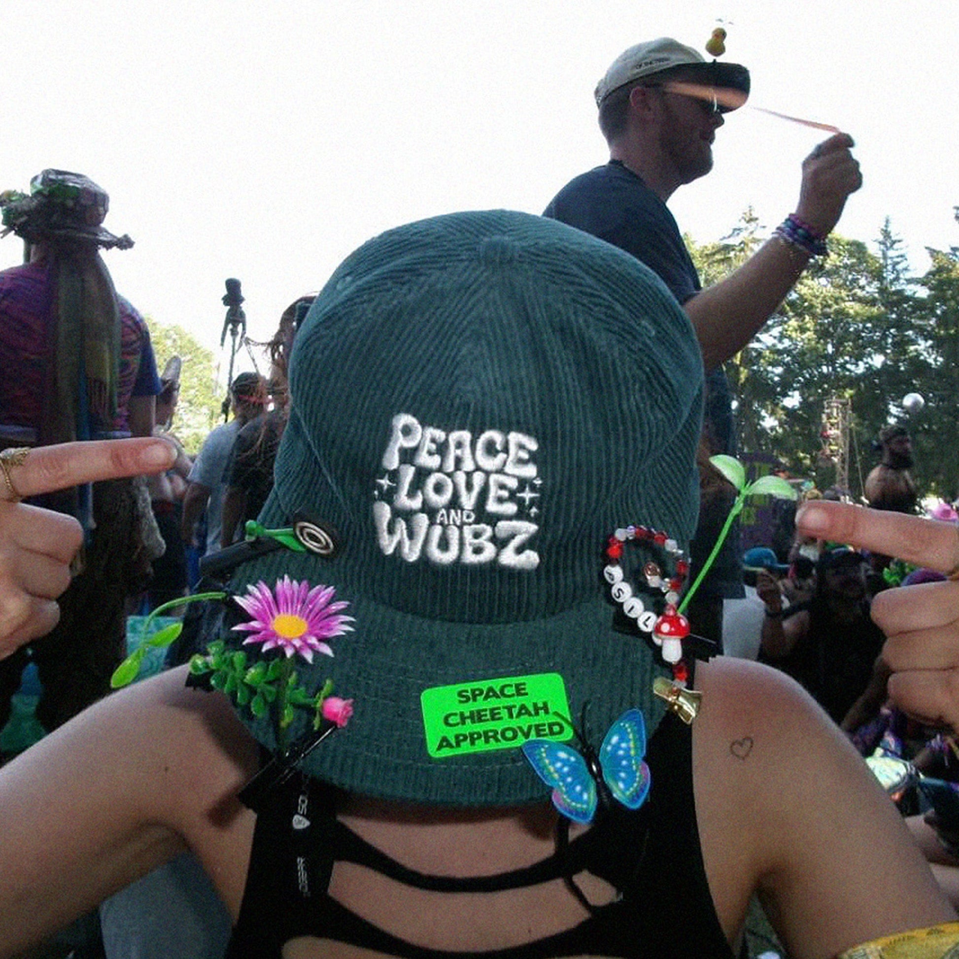 Person wearing a cap with 'Peace Love and Wubz' text at a music festival